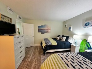 Ein Schlafzimmer mit einem Bett, einem Schminktisch, einem Fernseher und einem Surfbrett.