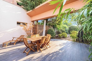Une terrasse extérieure avec une table et des chaises en bois, entourée de verdure et d’une clôture en bois.