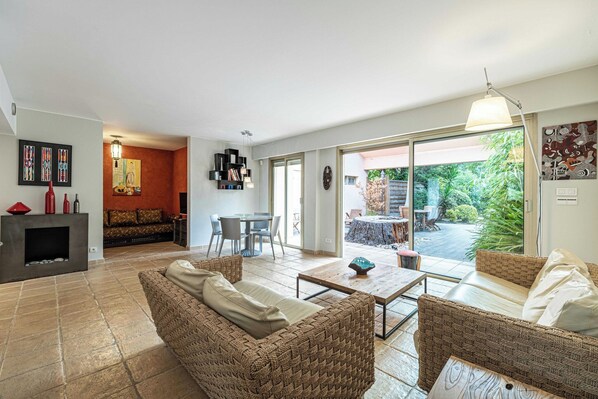 A modern living room with a fireplace, seating area, and a view of a garden. - Family Apartment with Pool & Garden 5 P - Cannes (Cannes)