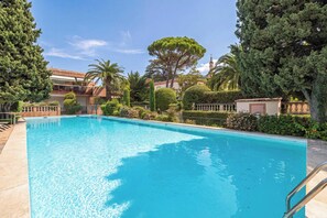 Une piscine entourée d’une végétation luxuriante et un bâtiment doté d’un balcon.