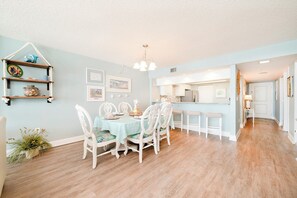 A dining area with a round table, white chairs, and a light blue tablecloth. There is a kitchen visible in the background. - Seychelles 605  2/2 Direct Oceanfront condo (Daytona Beach Shores)