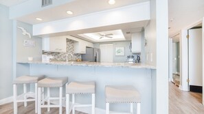 A kitchen with a central island, bar stools, and a ceiling fan. - Seychelles 605  2/2 Direct Oceanfront condo (Daytona Beach Shores)