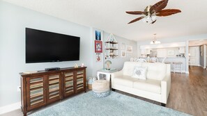 A living room with a flat-screen TV, a wooden cabinet, a white sofa, and a ceiling fan. - Seychelles 605  2/2 Direct Oceanfront condo (Daytona Beach Shores)