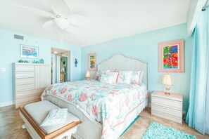 A bedroom with a bed, bedside tables, a bench, a ceiling fan, and artwork on the walls. - Seychelles 605  2/2 Direct Oceanfront condo (Daytona Beach Shores)