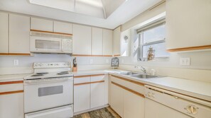 A compact kitchen with white cabinets, a microwave, stove, and a sink. - 606 Grand Coquina in Daytona Beach Shores, FL (Daytona Beach Shores)