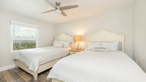 A bedroom with two beds, a ceiling fan, a nightstand with a lamp, and a window with a view. - 606 Grand Coquina in Daytona Beach Shores, FL (Daytona Beach Shores)