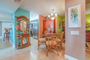A dining area with wicker chairs and a wooden table, a kitchen with a refrigerator, and a teal wall with a decorative mirror. - 6103 Towers in Ponce Inlet, FL (Ponce Inlet)