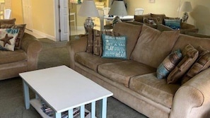 Ein Wohnzimmer mit einem braunen Sofa, einem weißen Couchtisch und einem blauen Kissen mit Text.