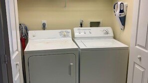 Une buanderie équipée de deux lave-linge et deux sèche-linge à chargement frontal, d’un sèche-mains fixé au mur et d’un panneau mural avec un thermostat.
