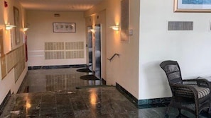 Un couloir d’hôtel avec un sol en marbre, un comptoir d’accueil et un fauteuil en osier.