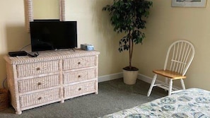 Ein Zimmer mit Fernseher auf einer Kommode, einem Sessel und einer Topfpflanze.