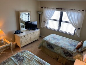 A bedroom with two beds, a dresser, a mirror, a lamp, and a window with curtains. - #705 Sandcastle 2/2 Oceanfront CondoTraffic Free Beach (Ponce Inlet)