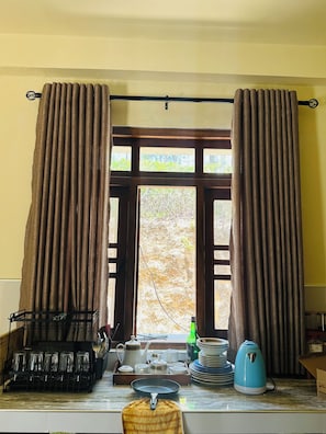 A kitchen with a window, curtains, a kettle, a tray with dishes, and a rack with glasses. - ELLA FOOD & BED (Ella)