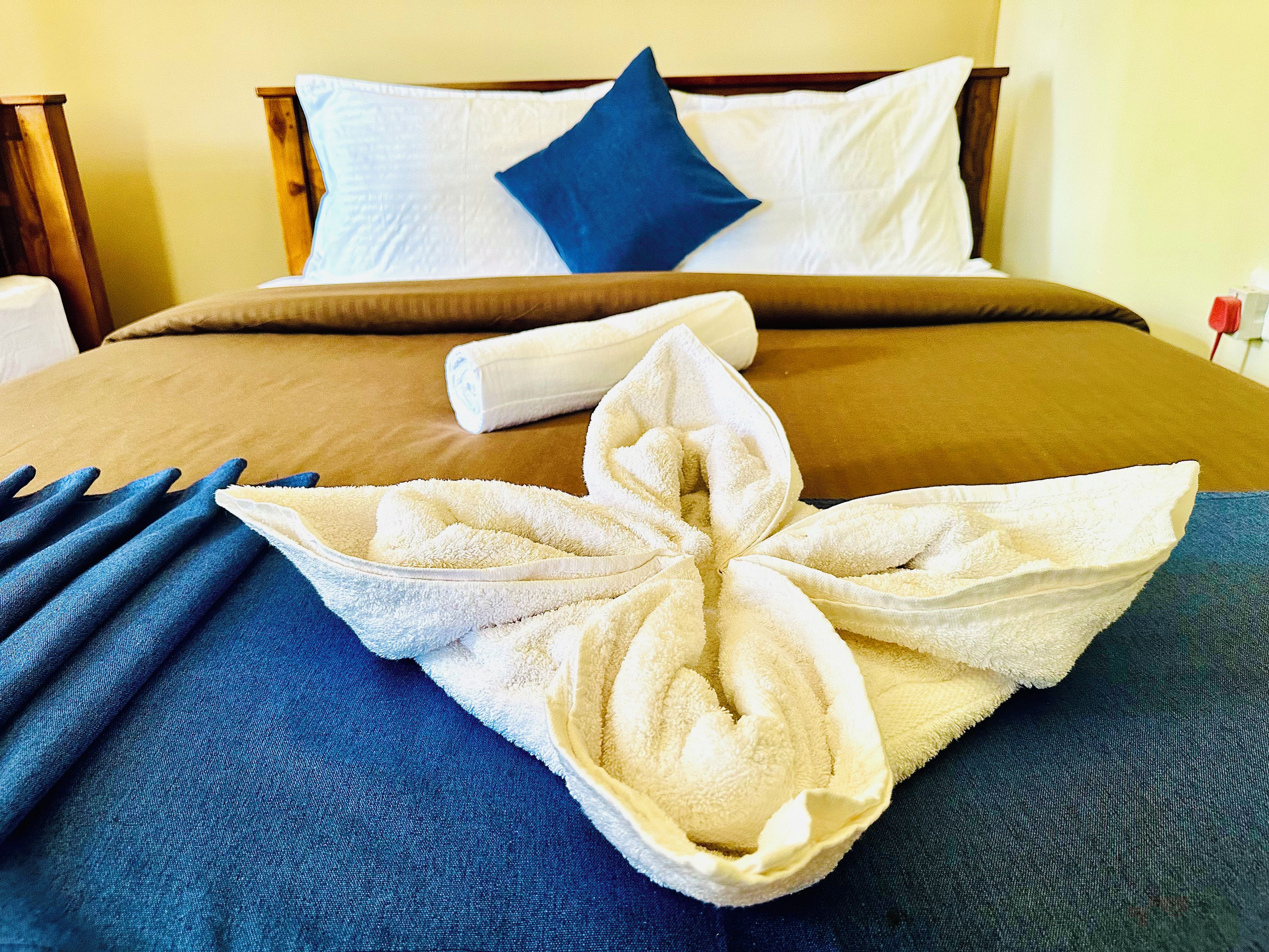 Una cama bien hecha con una decoración artística de toallas, una almohada azul y un cabecero de madera.