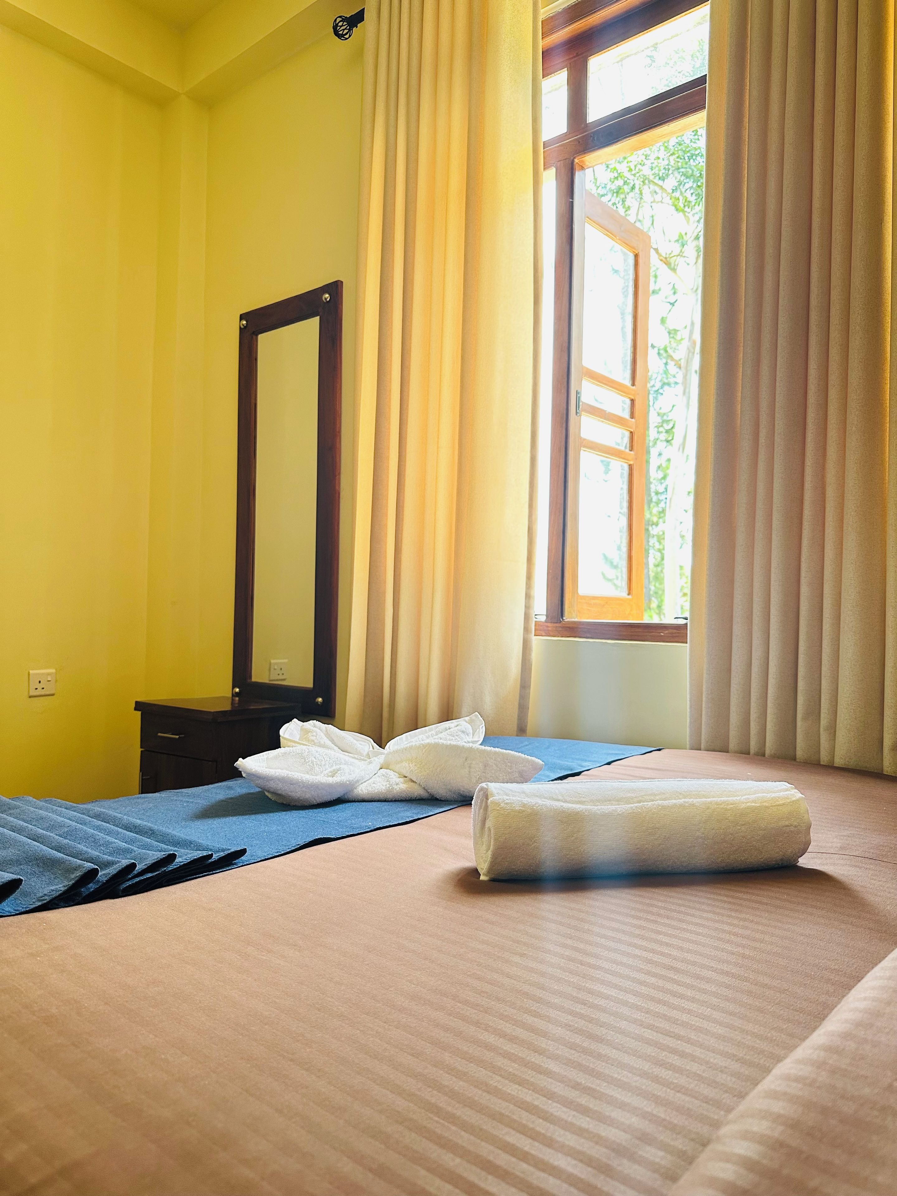 Habitació d'hotel amb llit, mirall i finestra amb cortines.