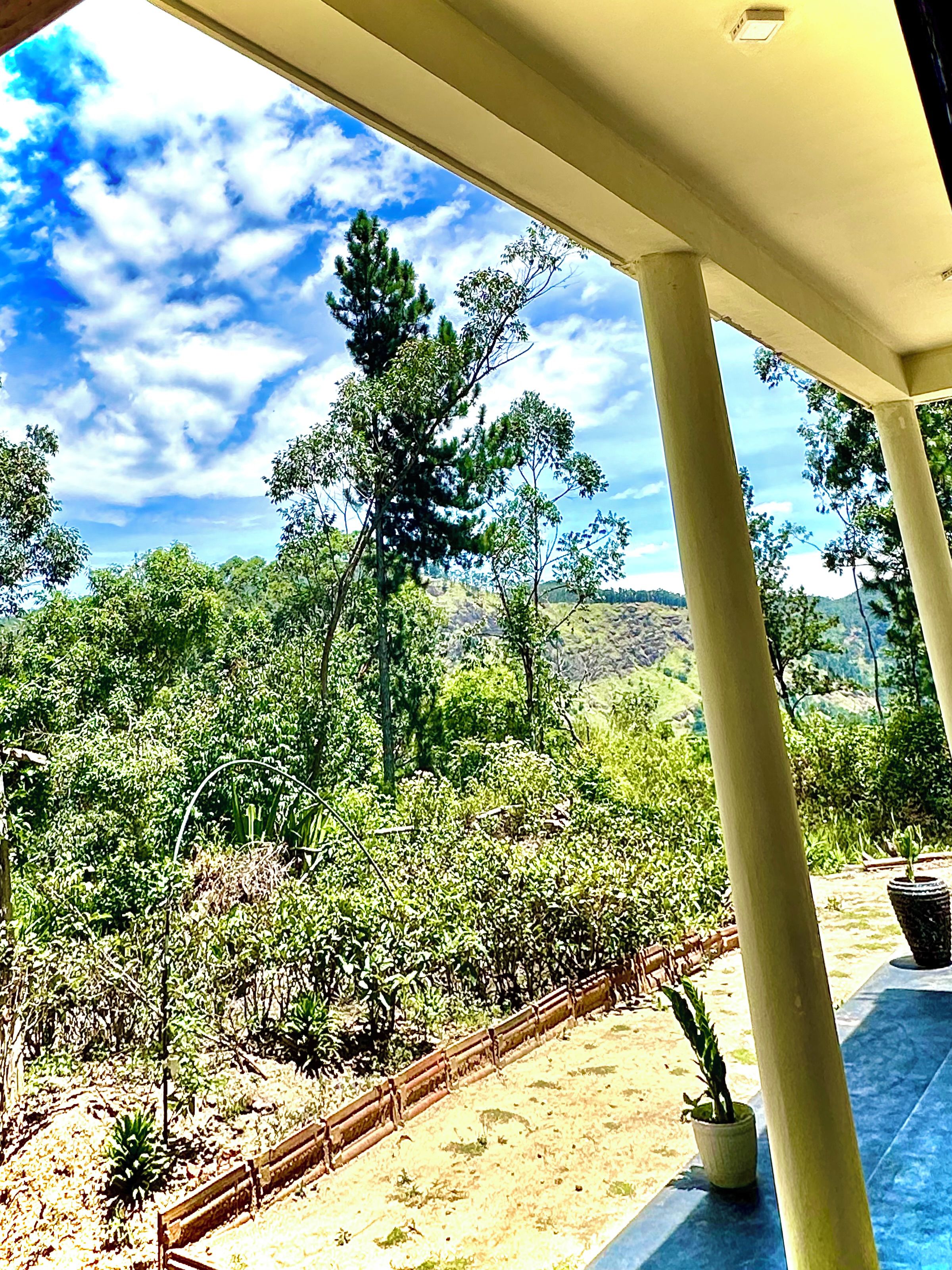 A covered outdoor area with a view of a landscaped garden and distant hills.