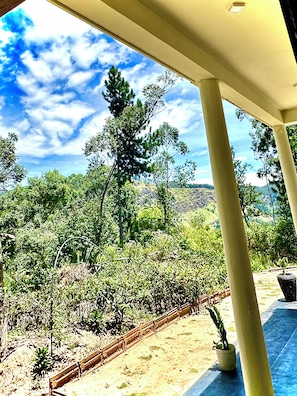 A covered outdoor area with a view of a landscaped garden and distant hills.
