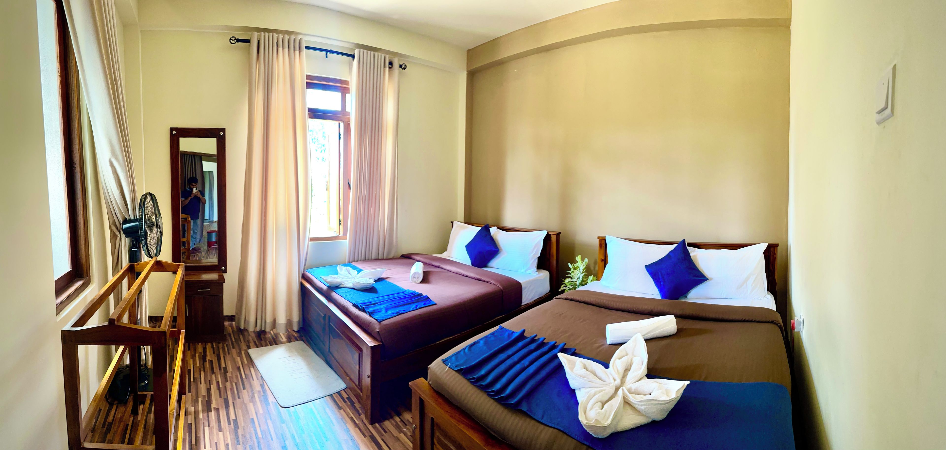 A hotel room with two beds, a wooden desk, a mirror, and a window with curtains.