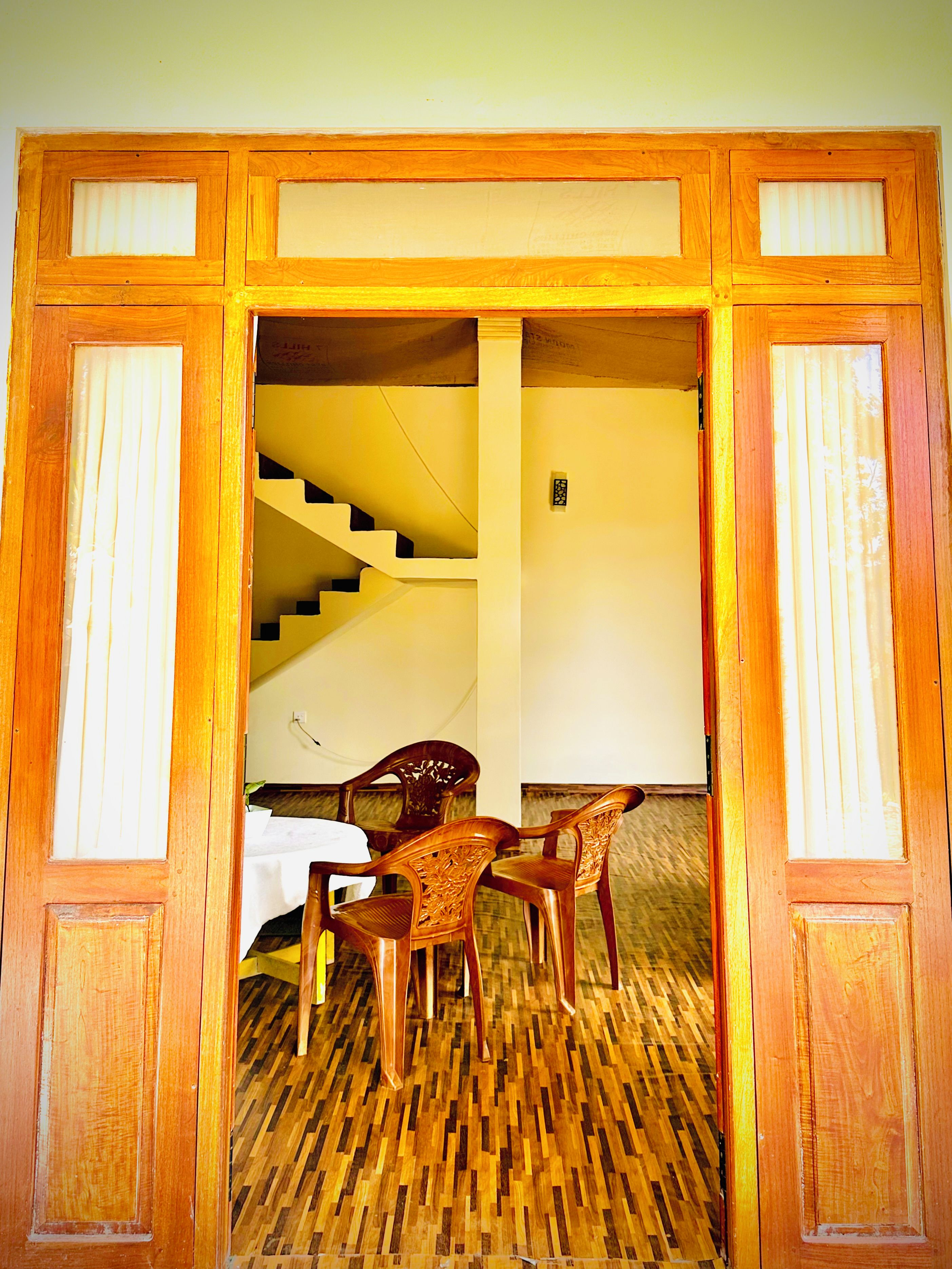 Un vano de madera que da a una habitación con una escalera, una mesa de comedor con sillas y un suelo de madera con diseño.