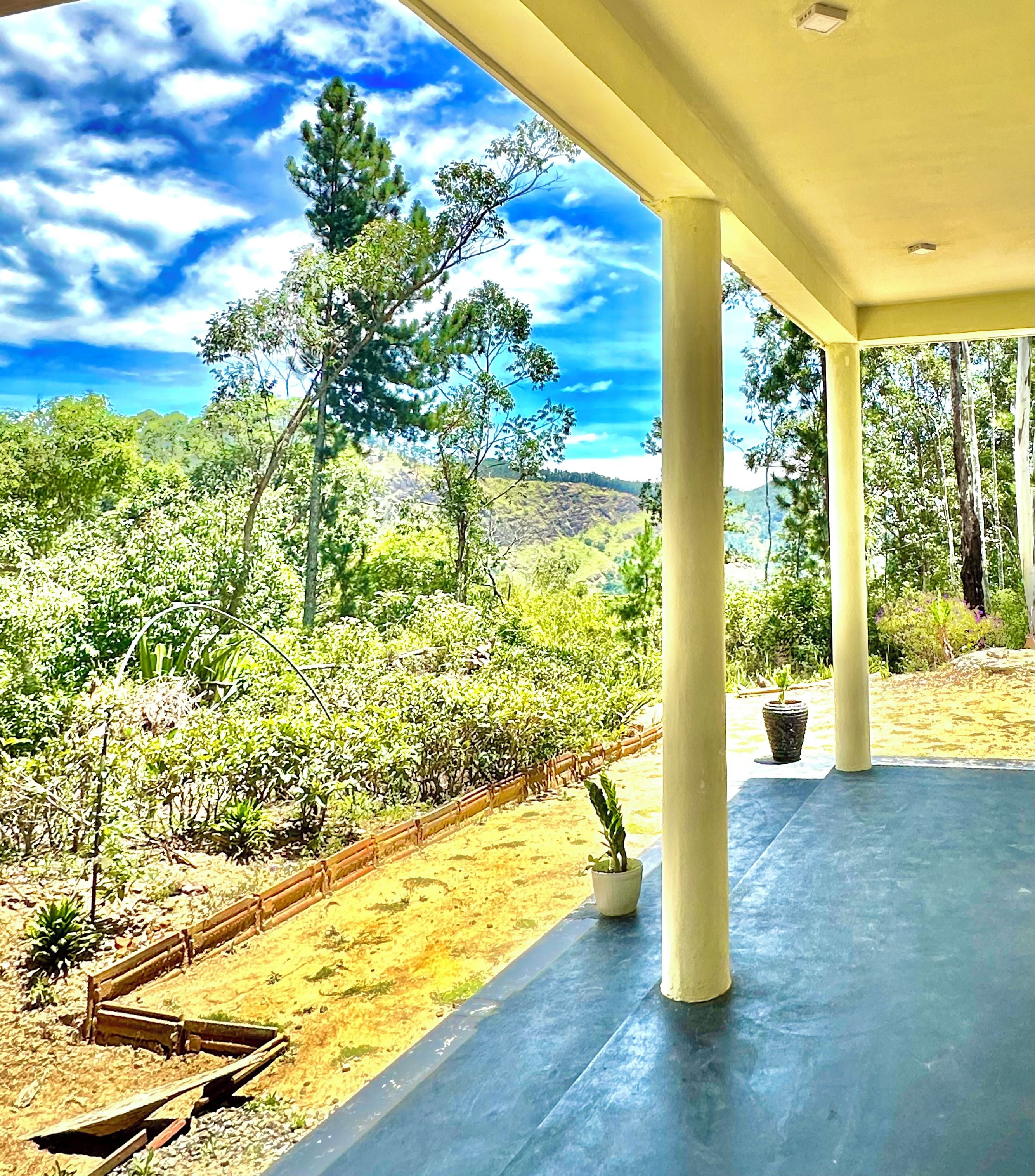A covered outdoor area with a view of a natural landscape, including trees and a hilly background.