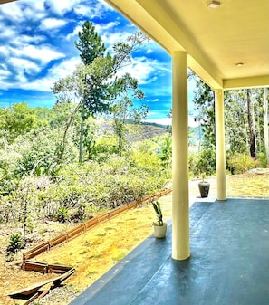 A covered outdoor area with a view of a natural landscape, including trees and a hilly background.