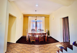 A dining area with a table set for four, a potted plant, and a view through a window with curtains. - ELLA FOOD & BED (Ella)