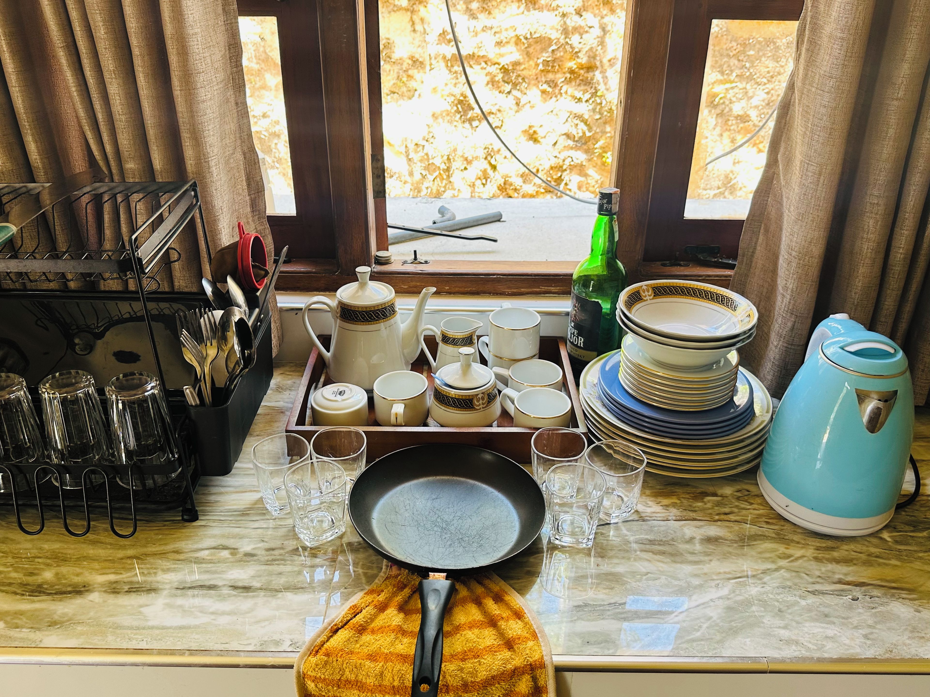Un piano di lavoro in cucina con un servizio da tè, bicchieri, piatti e un bollitore.