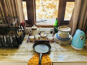 A kitchen counter with a tea set, glasses, plates, and a kettle. - ELLA FOOD & BED (Ella)