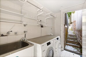 A laundry area with a washing machine, a sink, and shelves above. - Waterfall Garden 3-Bed Home McMahons Point (McMahons Point)
