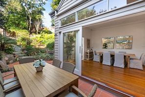 Ein modernes Haus mit einer Holzdielen-Terrasse, Sitzgelegenheiten im Freien und einem Garten.