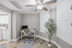 A room with a ceiling fan, a desk with a chair, a potted plant, and a window with blinds. - 707 Bella Vista in Daytona Beach Shores, FL (Daytona Beach Shores)