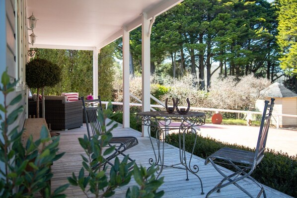 A covered outdoor seating area with wicker furniture and a metal table. - Charming 1-Bed Cottage in Historic Berrima (Berrima)