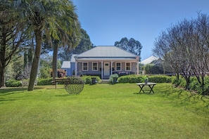 A house with a front porch, surrounded by a well-maintained lawn and trees. - Charming 1-Bed Cottage in Historic Berrima (Berrima)