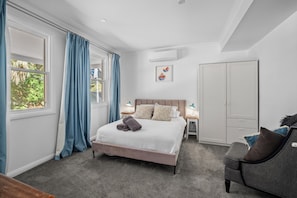 A bedroom with a bed, a wardrobe, a desk with a lamp, and a chair. - Charming 1-Bed Cottage in Historic Berrima (Berrima)