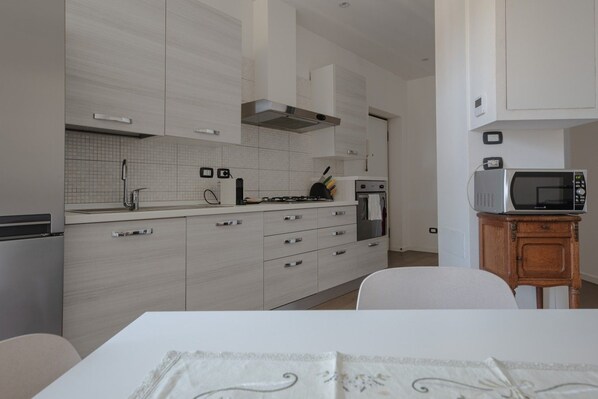 A modern kitchen with white cabinetry, a gas stove, an oven, and a microwave on a wooden side table. - Gulli 19 City Flat - 2 bdrs apartment (Parma)