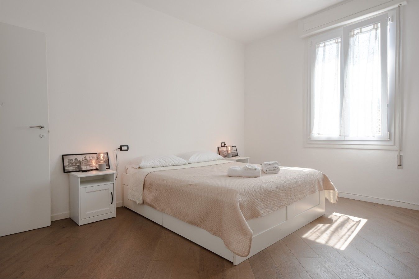 A minimalist bedroom with a bed, bedside tables, and a window.