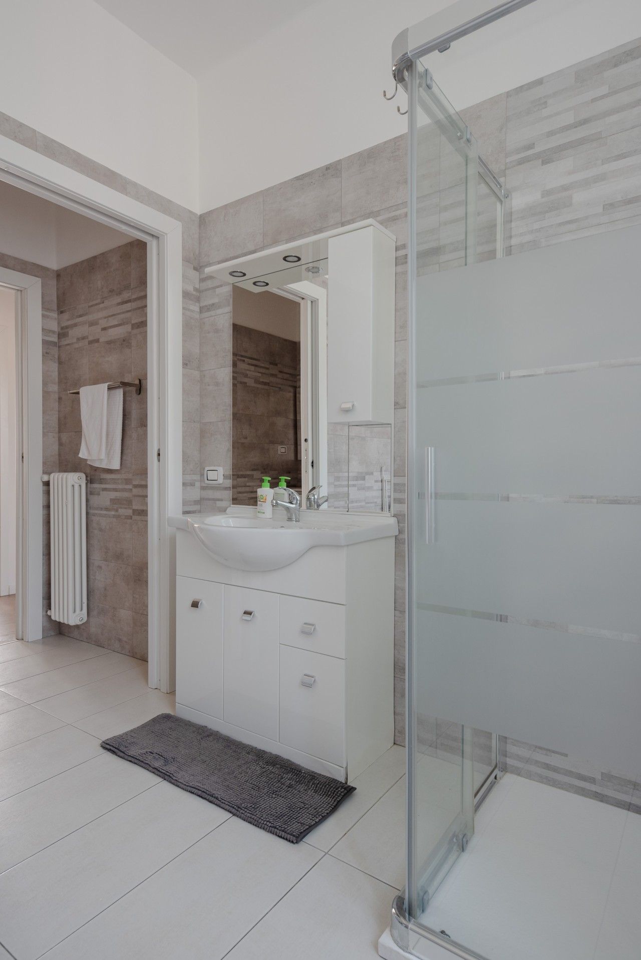 Un bagno moderno con cabina doccia in vetro, lavabo bianco con specchio sopra e portasciugamani.