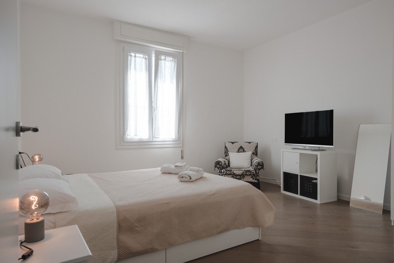 Ein schlicht eingerichtetes Schlafzimmer mit Bett, Sessel, Fernseher und einer Whiteboard-Tafel.