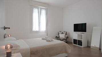Ein schlicht eingerichtetes Schlafzimmer mit Bett, Sessel, Fernseher und einer Whiteboard-Tafel.