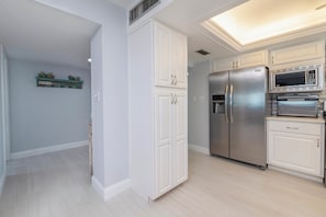 A modern kitchen with white cabinetry, a stainless steel refrigerator, and a built-in microwave. - 711 Sandcastle N in Ponce Inlet, FL (Ponce Inlet)