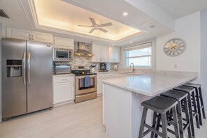 A modern kitchen with stainless steel appliances, a central island with bar stools, and a ceiling fan. - 711 Sandcastle N in Ponce Inlet, FL (Ponce Inlet)