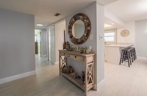 A hallway leading to a kitchen area with a wooden console table, a mirror, and a clock on the wall. - 711 Sandcastle N in Ponce Inlet, FL (Ponce Inlet)