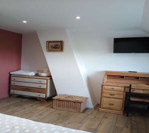 Ein Schlafzimmer mit einem hölzernen Schminktisch, einem Schreibtisch, einem an der Wand befestigten Fernseher und einem kleinen gerahmten Bild.