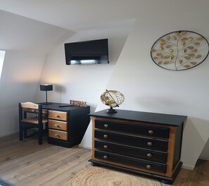 Ein Zimmer mit Schreibtisch, Kommode, Globus und einem an der Wand befestigten Fernseher.