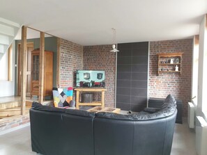 Ein Wohnzimmer mit einer schwarzen Ledersofa, einem Holz-TV-Schrank und einer Ziegelwand.