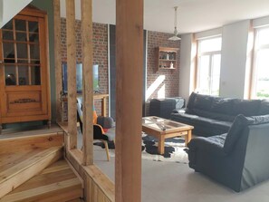 Un soggiorno con una scala in legno, un divano in pelle nera, un tavolino in vetro e una parete in mattoni.
