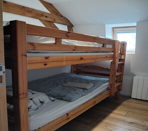A bunk bed with a wooden frame, a window with daylight, and a radiator on the floor. - 3-Bedroom Country Cottage at Chez Violette (STEENBECQUE)
