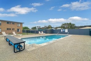 A swimming pool with lounge chairs and a table, surrounded by a fence and buildings. - Apollo Holiday Units - 2-Bed Unit in Narooma (Narooma)