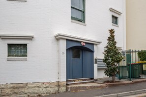 Ein weißes Gebäude mit einer blauen Tür, Hausnummer 35, und ein kleiner Baum davor.