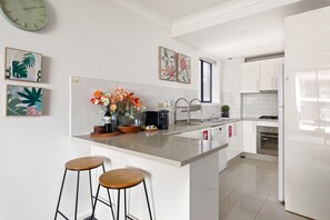 A modern kitchen with white cabinetry, a central island with stools, a sink, and a stove. - Spacious 2-Bed Apartment Near Parramatta CBD (Parramatta)